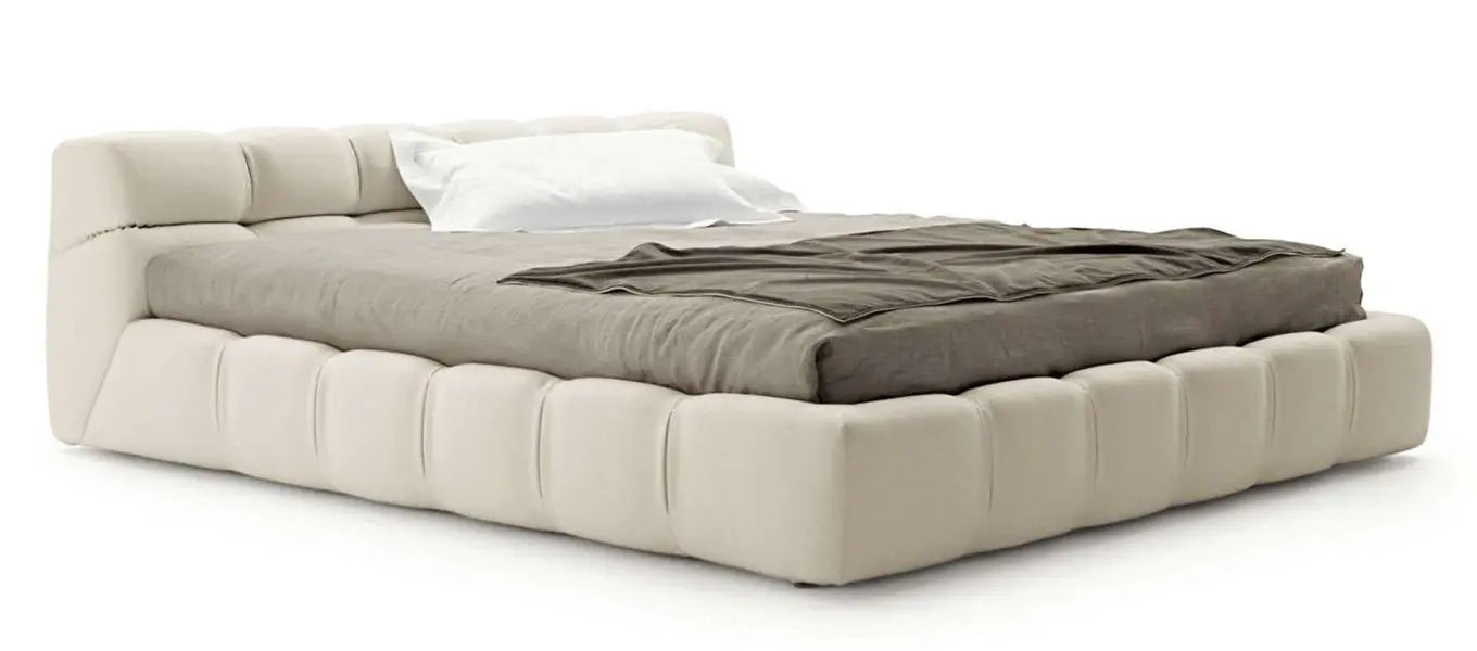 Experience the Modern Zen Bed, featuring a plush, tufted beige frame complemented by a neatly made gray blanket and a white pillow.