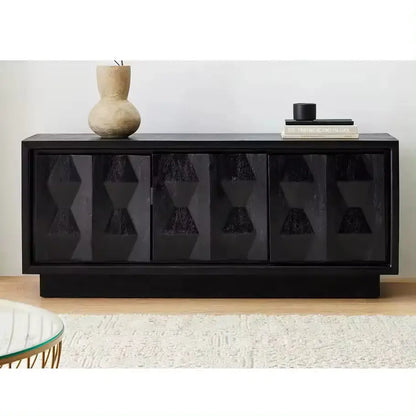 A Carved Pattern Black Media Console featuring geometric patterns on the doors, adorned with a vase and a black object on top, placed against a neutral wall and rug.