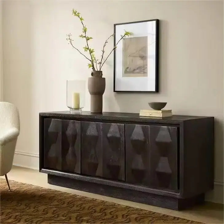 A Carved Pattern Black Media Console stands against a light-colored wall, adorned with a vase of branches, a framed picture, a candle in a glass holder, and a small bowl.