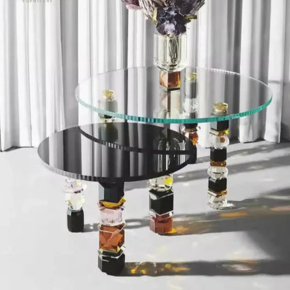 Two Luxury Glass Coffee Tables featuring modern design are placed in a well-lit interior. The larger table boasts a round glass top, while the smaller one has a black oval top, both complemented by abstract, geometric legs and adorned with floral centerpieces.