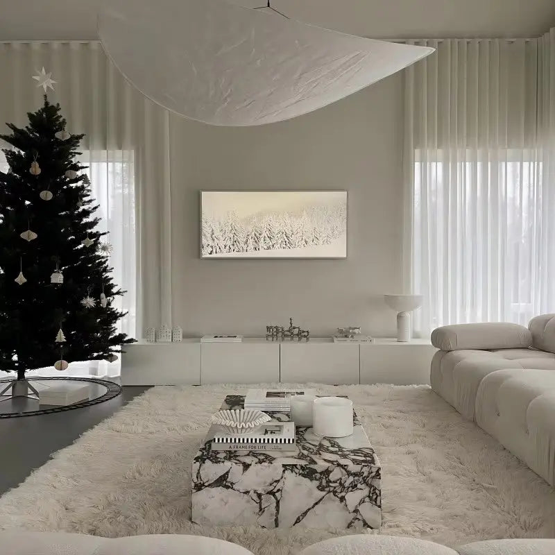 Minimalist living room featuring a decorated Christmas tree, Calcutta Viola Marble Coffee Table, shag rug, and neutral tones. A large abstract ceiling fixture and landscape artwork complete the space.