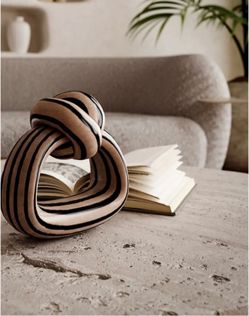 A sculptural Nordic Lob Low Table rests on a table beside a stack of books, with a couch and plant in the background.