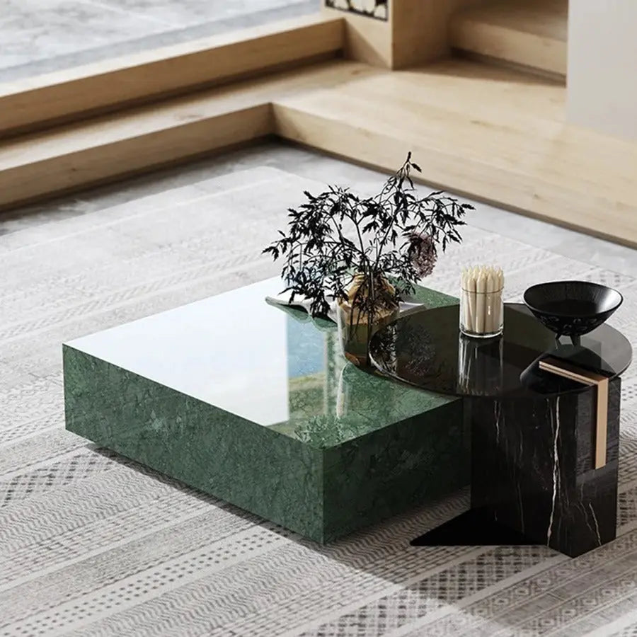 A modern living room with a Modern Green Marble Top Coffee Table adorned with decorative branches and a black vase, placed on a patterned area rug by a large window.