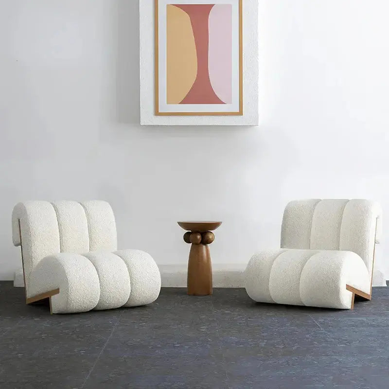 Two Ella Leisure Chairs, featuring modern white upholstery and sleek curved designs, are placed on either side of a small wooden side table. A framed abstract art piece hangs on the wall behind them.